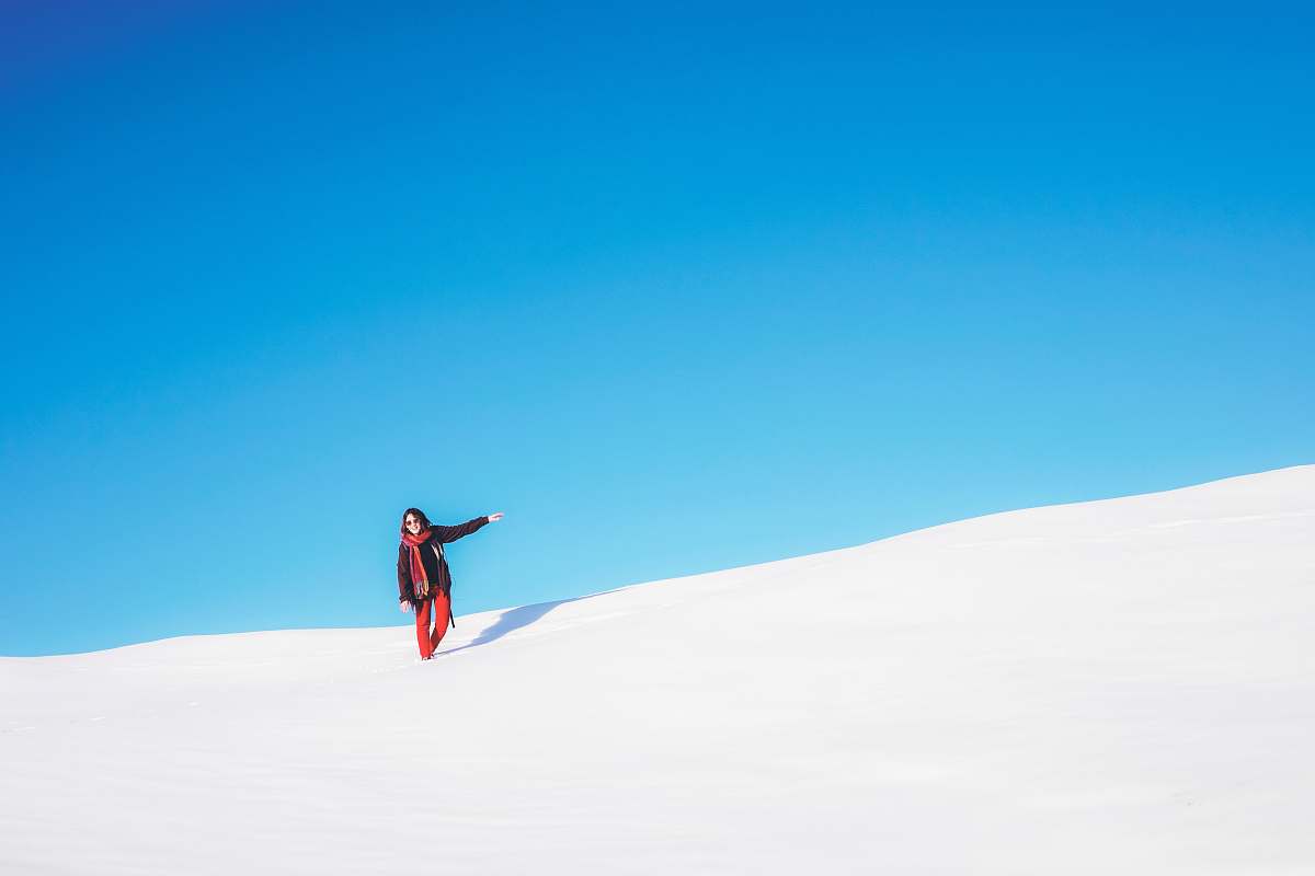 white sand woman standing on white snow field during daytime blue